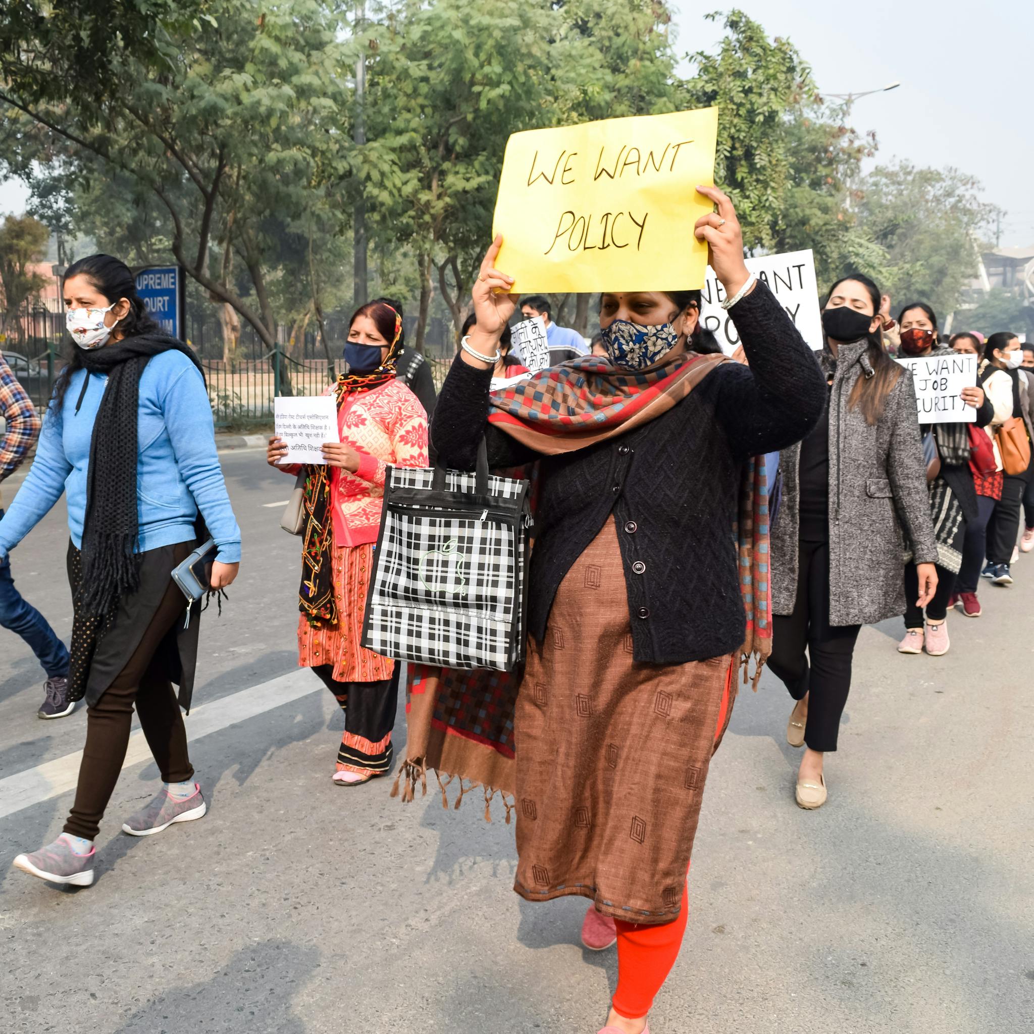 A group of masked protesters marching with signs demanding policy changes.