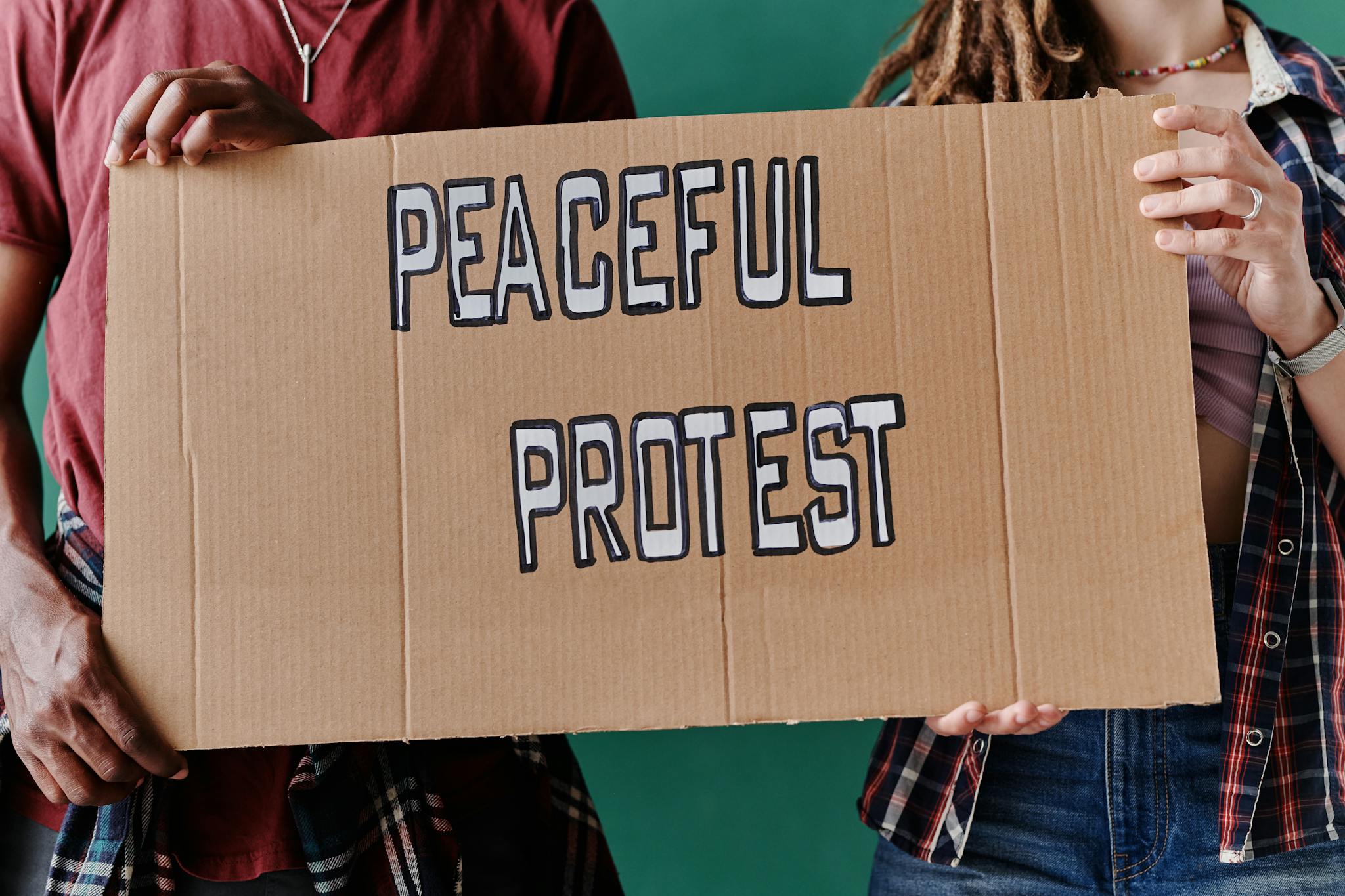 Activists hold a cardboard sign advocating for a peaceful protest, emphasizing social justice.