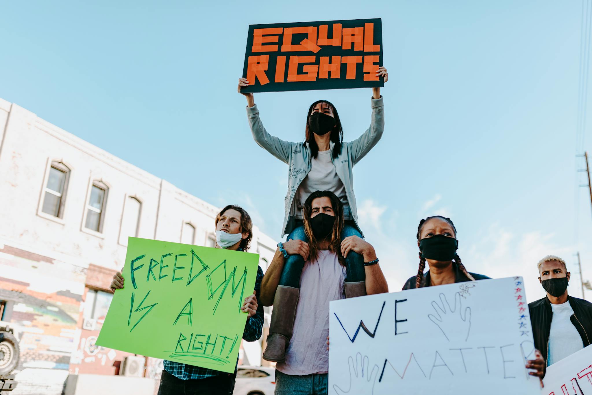 Diverse group of masked protesters holding signs for equality and rights outdoors.
