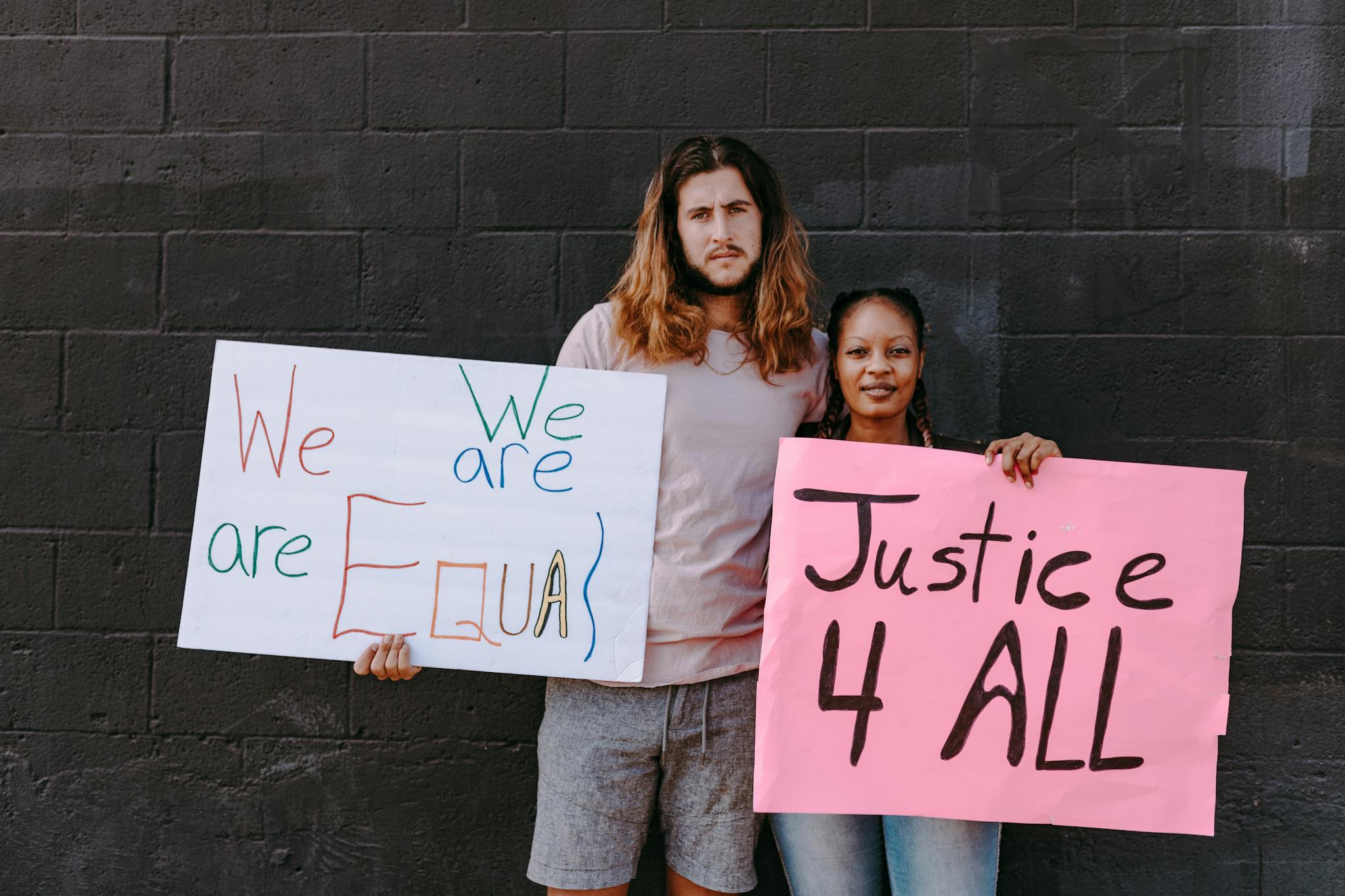 Two people holding equality and justice protest signs against a dark wall.
