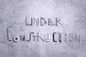 Under construction text creatively formed using various screws and tools on a concrete background.